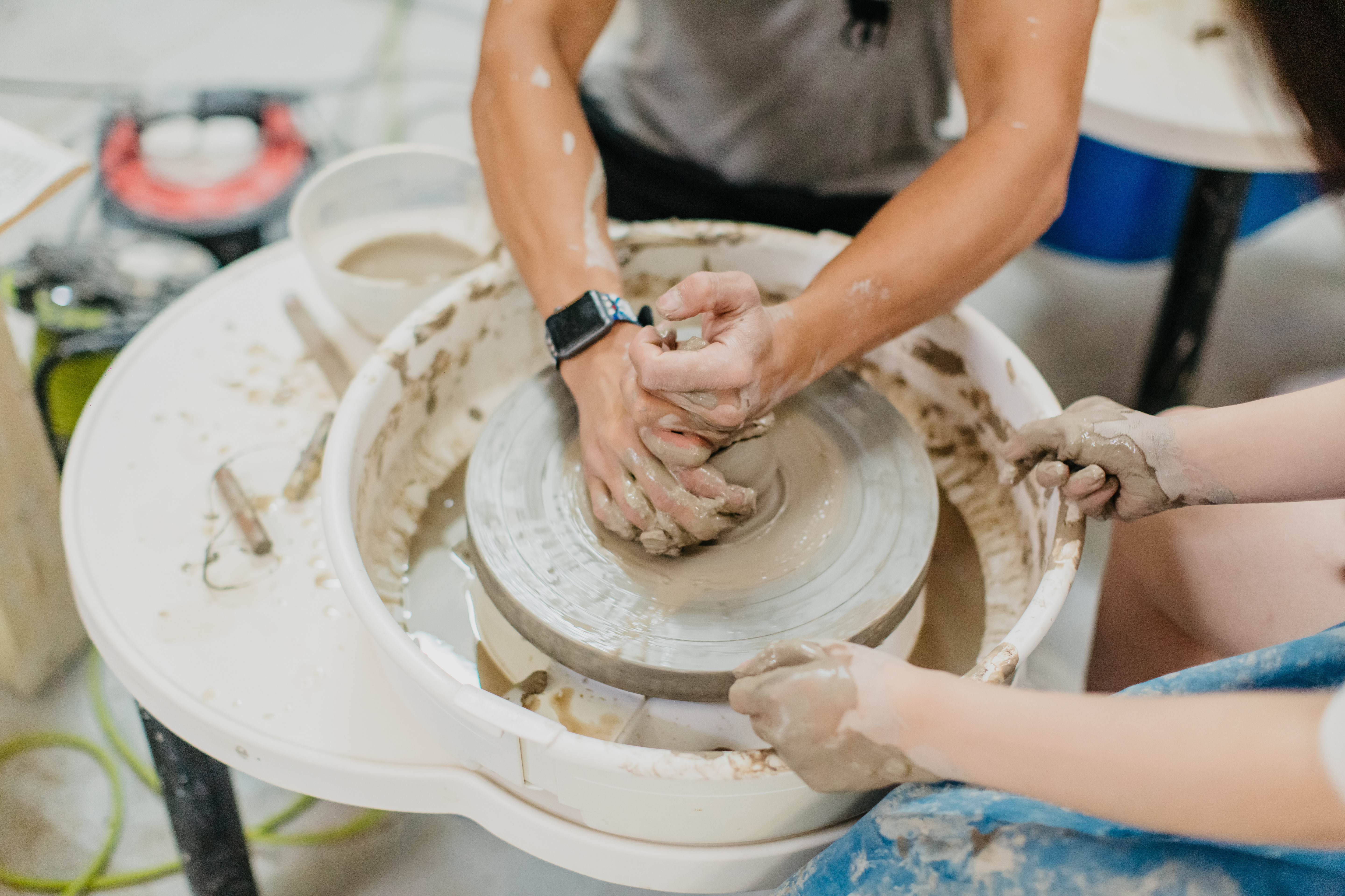 Two people helping each other to throw a pot on a wheel